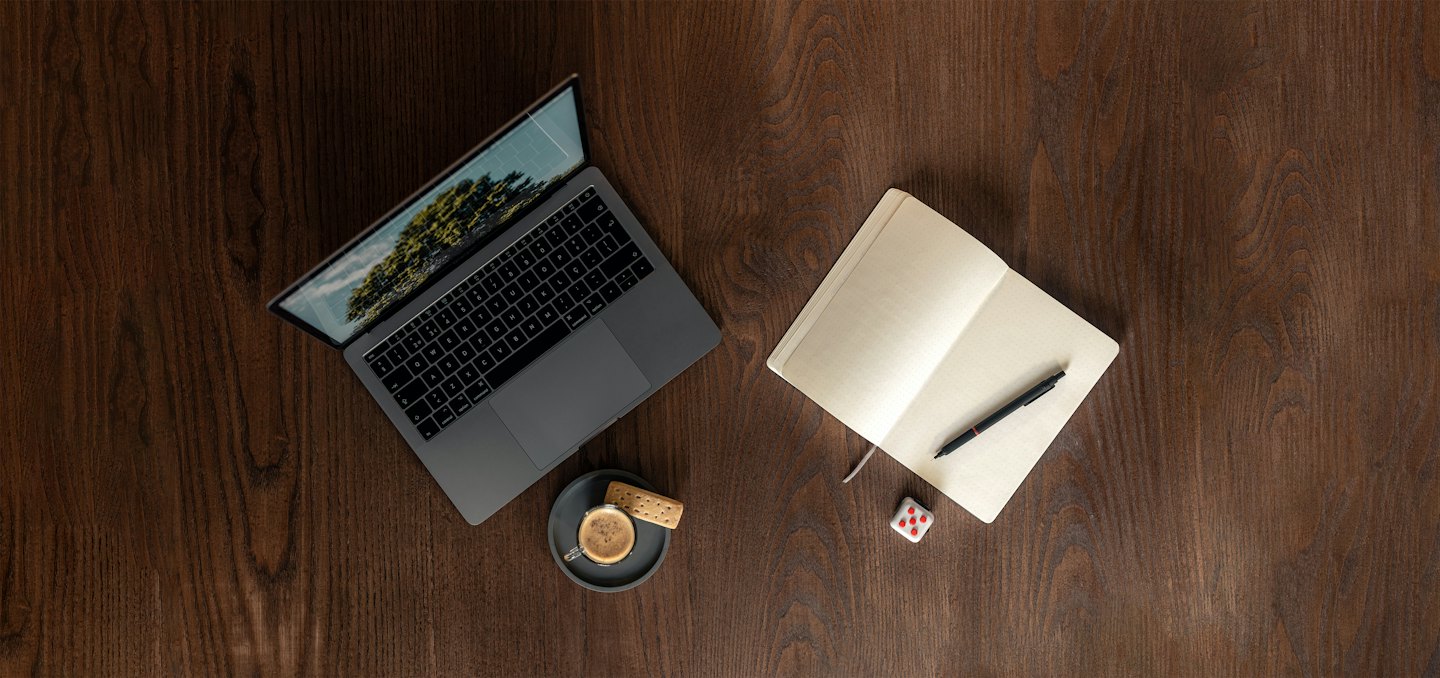 Laptop, Notizbuch und Kaffee stehen auf einem Holztisch.