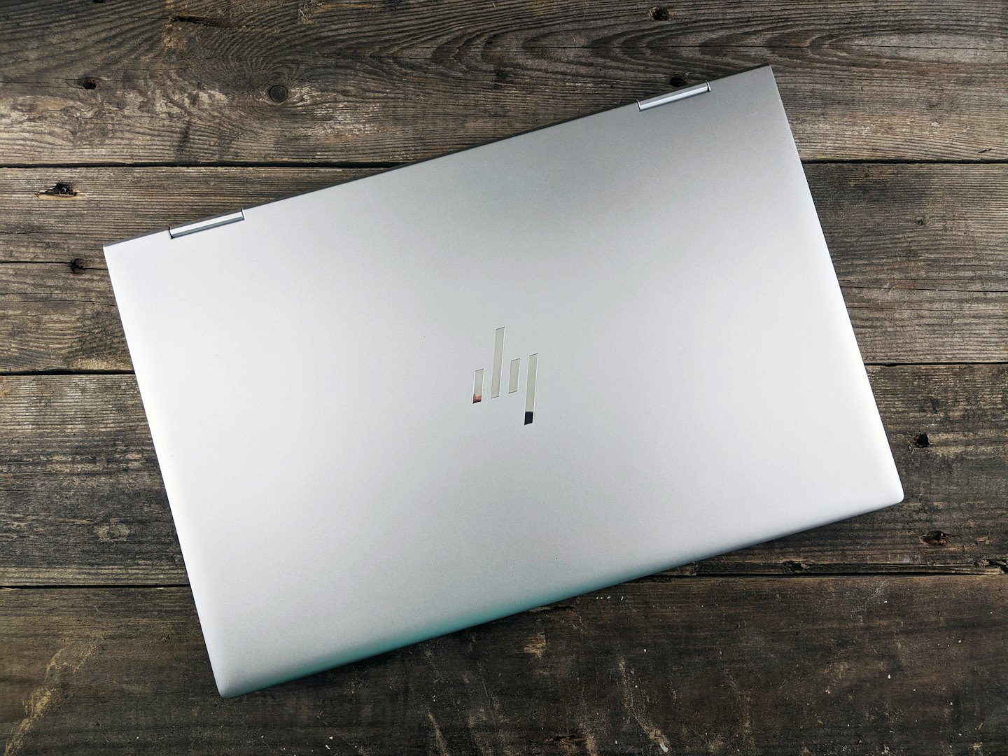 Ein geschlossener silberner Laptop liegt auf einem rustikalen Holztisch.