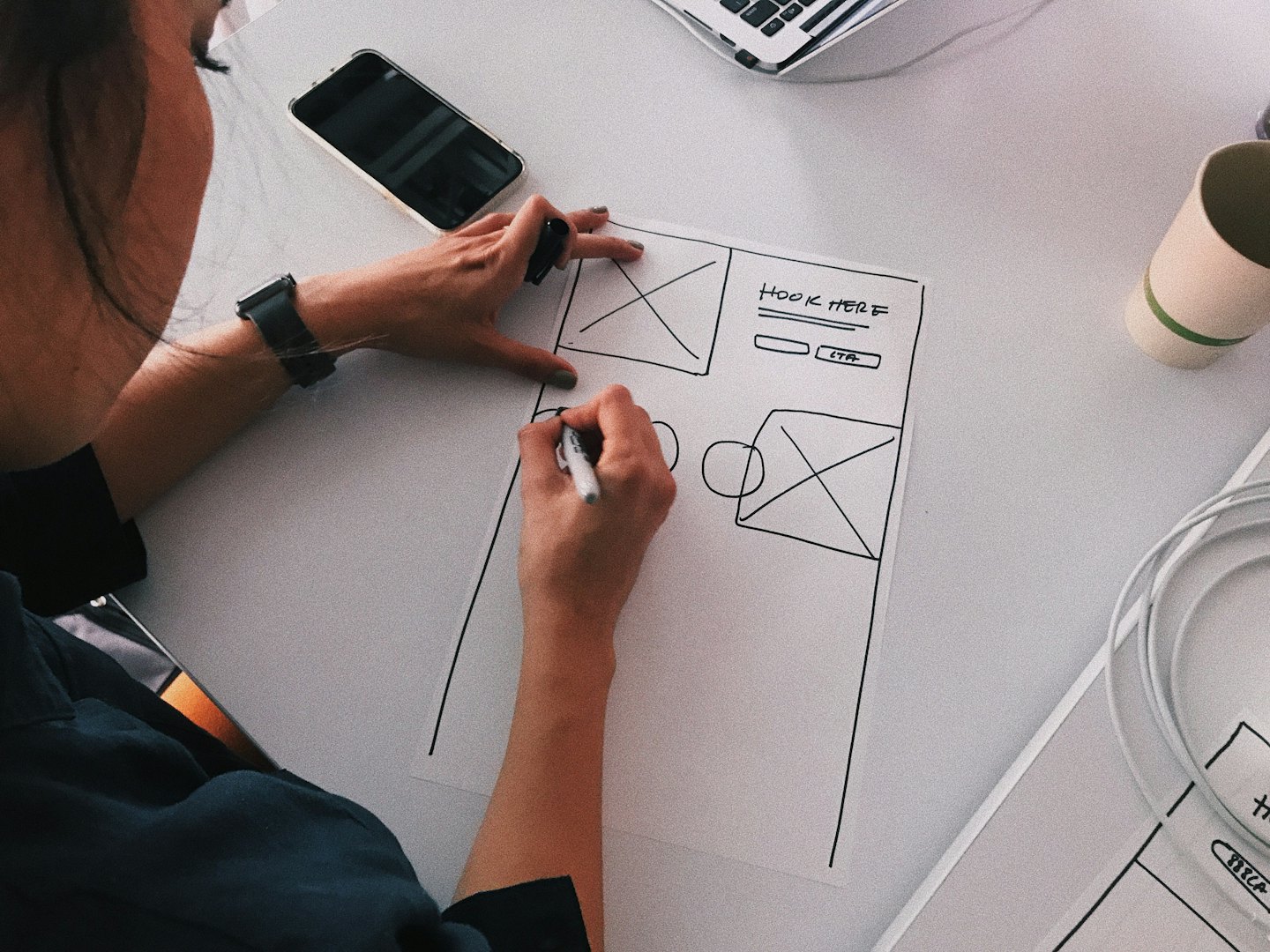 Designer skizziert Website-Wireframe mit Beschriftungen auf dem Schreibtisch.